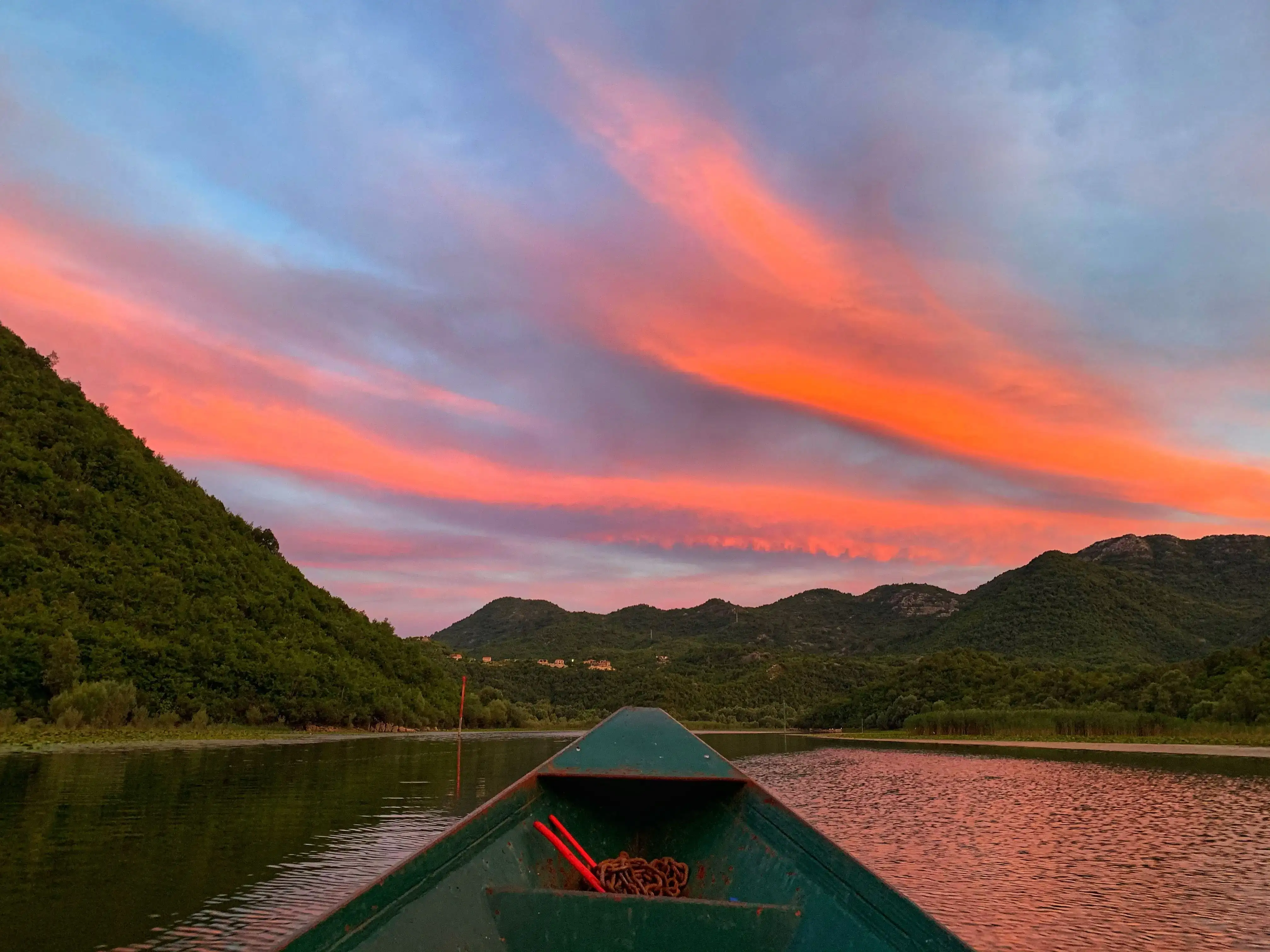 Boat tour on Skadar Lake at sunset with mountains reflected in still water
